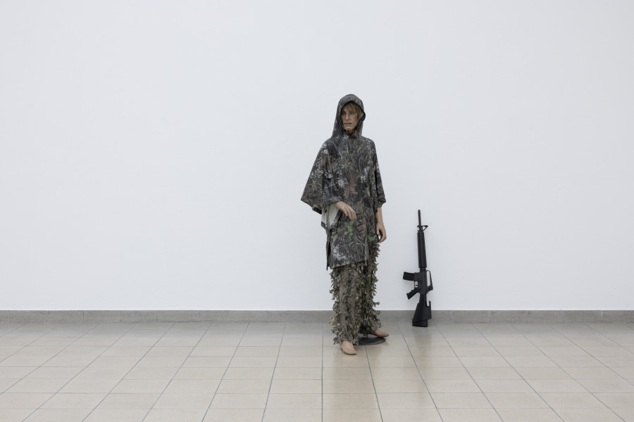 John Miller, Richard Hoeck, Camouflage on a Mannequin (male mannequin), 2008, Schaufensterpuppe, Kunststoff-Regenmantel mit militärischem Tarnmuster, Kunststoffhose, Kunststoffblätter-Tarnanzug, Automatische Schusswaffe / Mannequin, plastic raincoat with military camouflage pattern, plastic trousers, plastic leaf camouflage suit, automatic firearm. Dimension der Installation variabel / installation dimensions variable. Courtesy the artists. Photo: Gina Folly