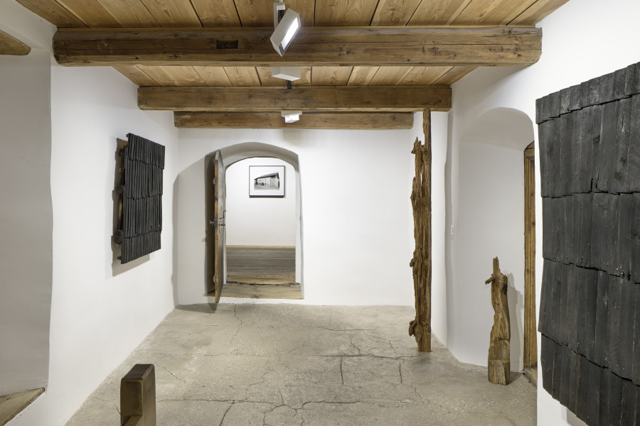 Exhibition view, Augustas Serapinas, Roof of a House from Steponių Village, 2022, charred reclaimed wooden shingle roof, Part of the House from Skirgiškės, 2022, reclaimed wood. Photo: Ralph Feiner, Courtesy of the artist and Galerie Tschudi