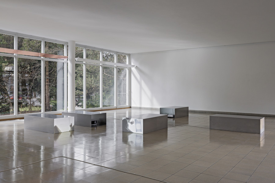 Nolan Lucidi, Bildersaal, Installation view Kunsthaus Glarus. Photo: Gina Folly, Kunsthaus Glarus 2026. Screening Sculpture (1–10), 2026, 10-Kanal-HD-Videoinstallation, Ton, verschiedene Längen zwischen 00:48 Min. und 26:37 Min., Loop, Gel-Transfer, Papierreste, Rückprojektionsfolie, Vorhang, Edelstahl. Metallobjekte jeweils 70 × 40 × 140 cm. Views (Loveroom 1-6), 2026, Bronze- und champagnerfarbene, verspiegelte Anti-Voyeur-Folie auf der Einfassung der Leuchten. 448,5 × 18,6 cm, 420 ×18,6 cm. Courtesy the artist