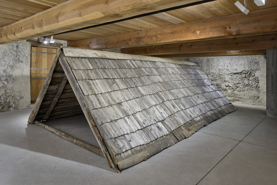 Exhibition view, Augustas Serapinas, Upper Roof Part of the House from Steponių Village, 2022, charred reclaimed wooden shingle roof, 180 x 640 x 340 cm. Photo: Ralph Feiner, Courtesy of the artist and Galerie Tschudi