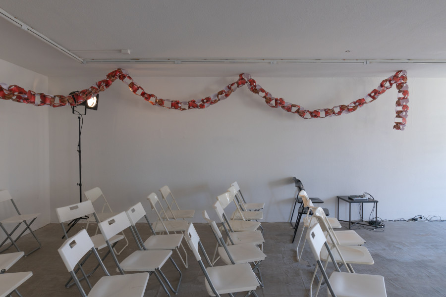 Exhibition view, Sven Gex, celebratory, Halmet, Zürich, 2025. From top to bottom: Sven Gex, garland for ‚celebratory‘ (maid-of-all-work character), 2025, hand cut printed pictures, staples ; Sophie Becker, Setup of “Ronnie’s World”, Performance during the opening night