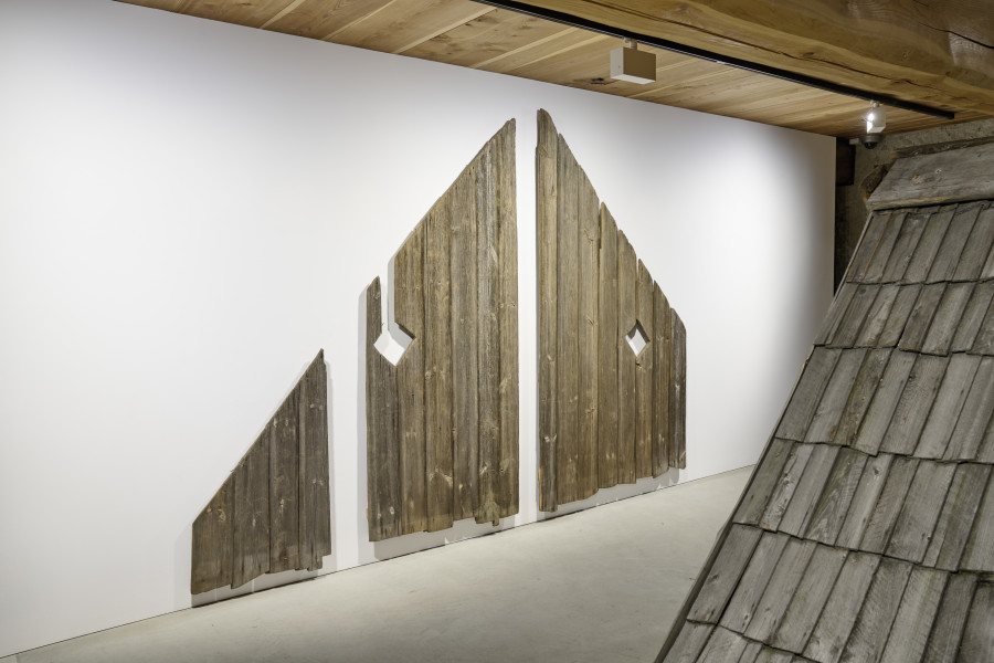 Exhibition view, Augustas Serapinas, Pediment from an Unknown House, 2022, reclaimed wood, 222 x 330 x 5.5 cm, Upper Roof Part of the House from Steponių Village, 2022, charred reclaimed wooden shingle roof, 180 x 640 x 340 cm. Photo: Ralph Feiner, Courtesy of the artist and Galerie Tschudi
